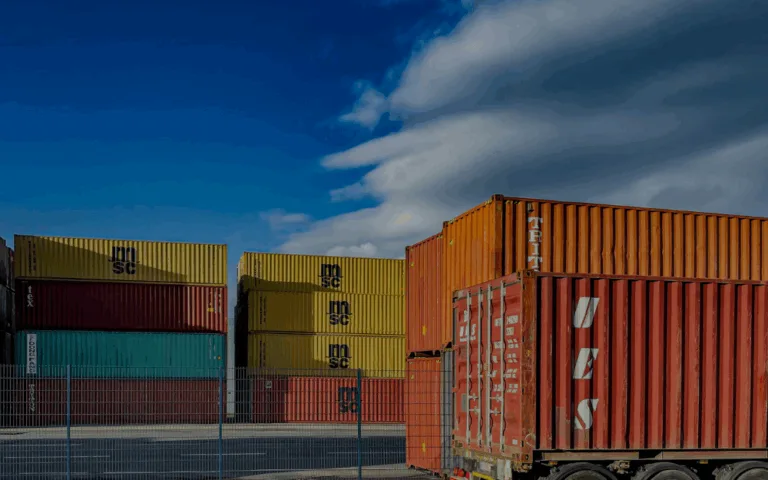 Stacked shipping containers at a busy port, illustrating global logistics supply chains