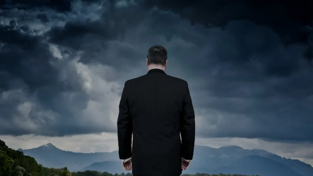 Business professional standing with back turned, facing a dark, stormy sky, symbolizing economic weather risk.